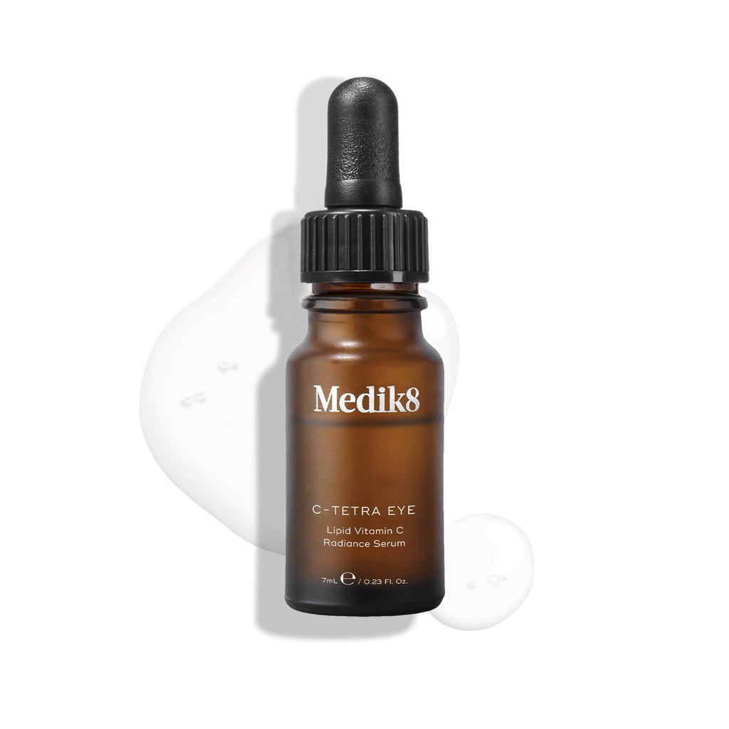 Fľaštička séra Medik8 C-Tetra Eye Lipid Vitamin C Radiance Serum na bielom pozadí s priehľadnými kvapôčkami séra, ktoré zdôrazňujú jeho tekutú konzistenciu.