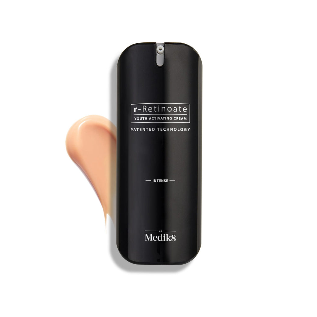 Fľaštička Medik8 r-Retinoate Intense Youth Activating Cream je zobrazená na bielom pozadí s viditeľným vzorkom broskyňovo sfarbenej krémovej textúry za ňou.
