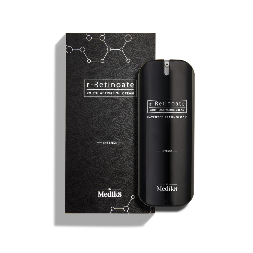 Fľaštička Medik8 r-Retinoate Intense Youth Activating Cream stojí vedľa svojho čierneho vonkajšieho obalu s bielymi hexagonálnymi chemickými štruktúrami a textúrovaným vlnitým vzorom.
