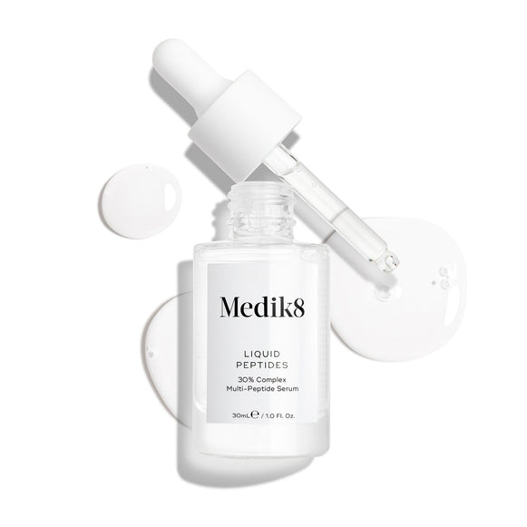 Priehľadná sklenená fľaštička séra Liquid Peptides je zobrazená s vybratým kvapkadlom, ktoré leží vedľa nej spolu s kvapkami séra, ktoré detailne ukazujú jeho tekutú textúru.-15