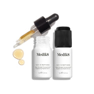 Vedľa dvoch malých bielych fľaštičiek séra stojí biela kartónová krabička s produktom Medik8 Oxy-R Peptides. Jedna fľaštička má čiernu kvapkadlo, druhá čierny uzáver.