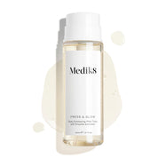Fľaša tonika Medik8 Press & Glow stojí na čistom bielom pozadí, na ktorom sú viditeľné priesvitné kvapky tekutiny a kaluž, čím sa zdôrazňuje jej vodnatá konzistencia. Text uvádza, že ide o 200 ml tonikum Daily Exfoliating PHA Tonic s enzýmovým aktivátorom. 