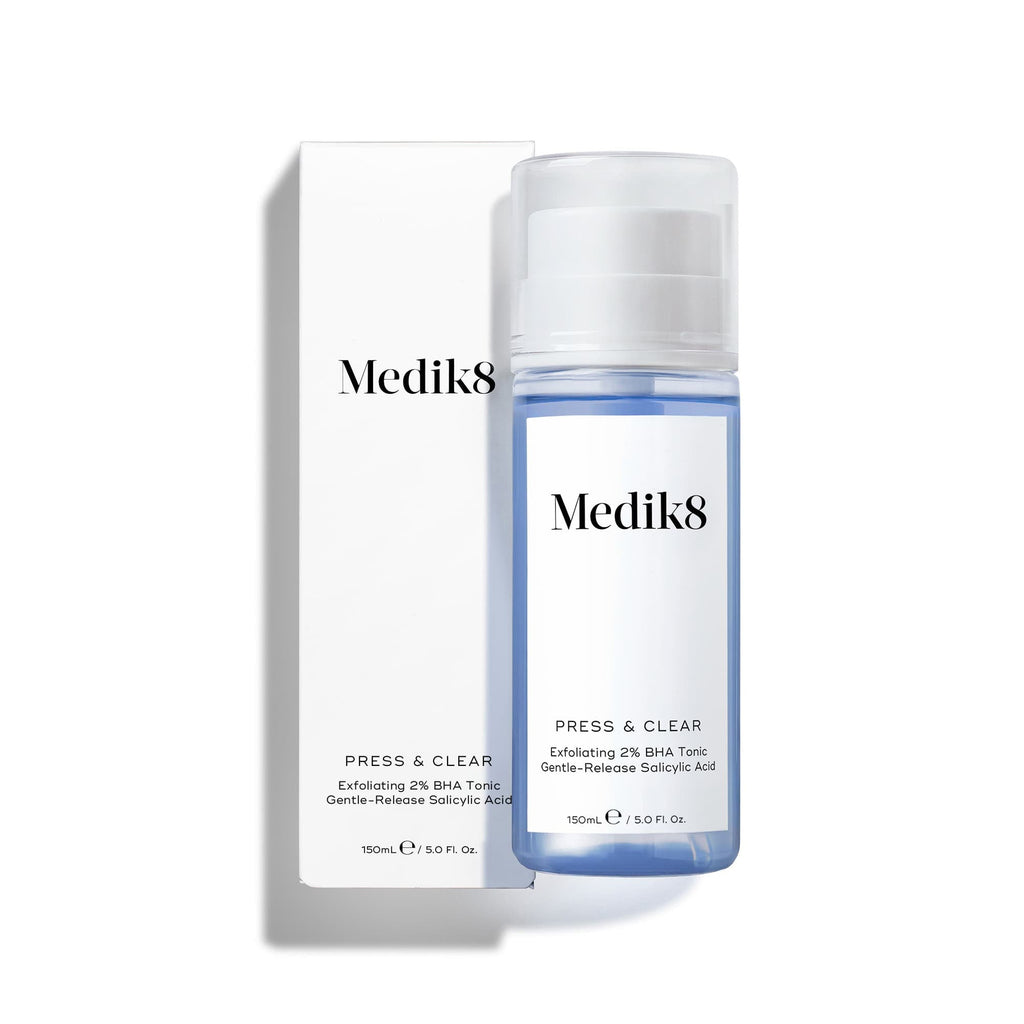 Fľaša Medik8 Press & Clear s modrou tekutinou stojaca vedľa bielej krabičky. Nápis ju označuje ako  exfoliačné tonikum s 2 % BHA  s  kyselinou salicylovou s postupným uvoľňovaním. 