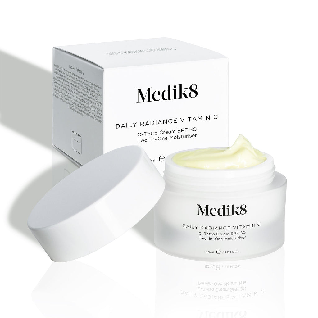 Otvorený kelímok krému Daily Radiance Vitamin C je zobrazený pred kartónovým obalom produktu, pričom je viditeľná textúra krému.
