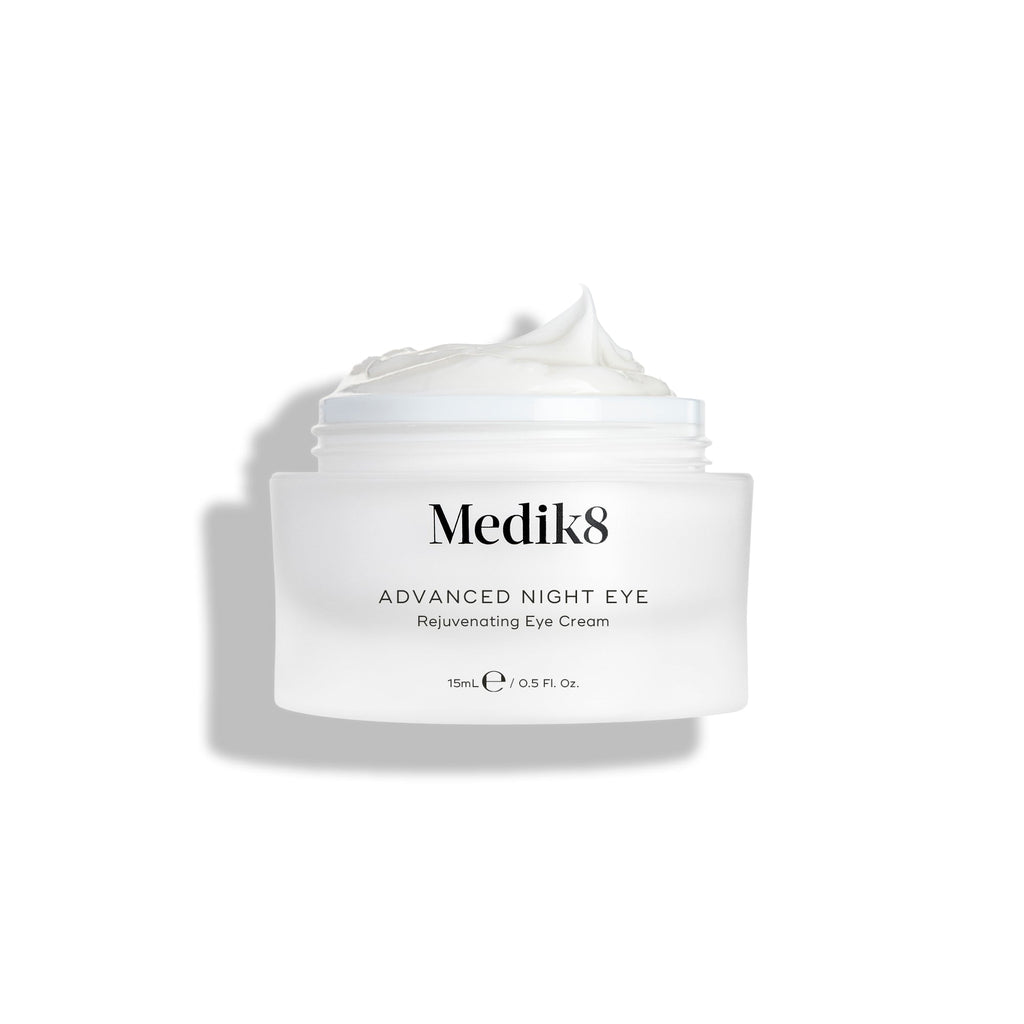 Kelímok nočného očného krému Medik8 Advanced Night Eye Cream stojí na bielom pozadí so снятым viečkom. Bohatý biely krém je viditeľný vo vnútri kelímka a zvýrazňuje svoju textúru.
