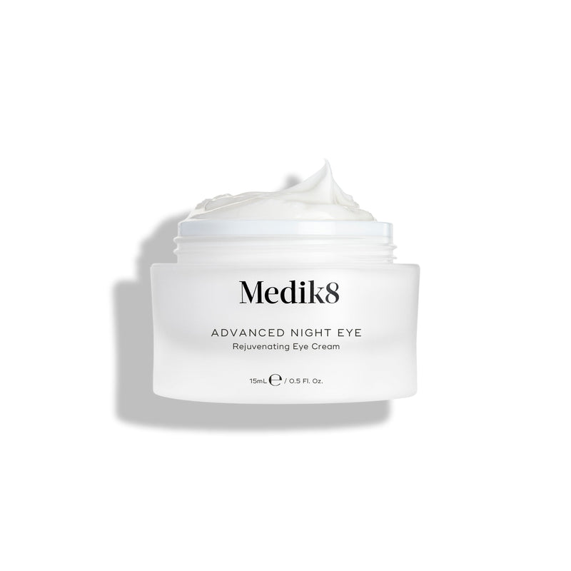 Kelímok nočného očného krému Medik8 Advanced Night Eye Cream stojí na bielom pozadí so снятым viečkom. Bohatý biely krém je viditeľný vo vnútri kelímka a zvýrazňuje svoju textúru.
