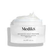 Otvorený téglik krému Medik8 Advanced Night Restore s bohatou kôpkou bieleho krému s vyformovanou špičkou na vrchu, zobrazený na čistom bielom pozadí, ktoré zvýrazňuje jeho hladkú, obnovujúcu textúru. Čierny text na tégliku hovorí: Rejuvenating Multi-Ceramide Night Cream.