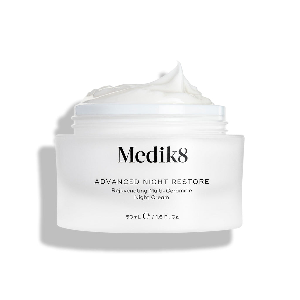 Otvorený téglik krému Medik8 Advanced Night Restore s bohatou kôpkou bieleho krému s vyformovanou špičkou na vrchu, zobrazený na čistom bielom pozadí, ktoré zvýrazňuje jeho hladkú, obnovujúcu textúru. Čierny text na tégliku hovorí: Rejuvenating Multi-Ceramide Night Cream.