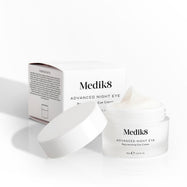 Otvorený kelímok očného krému Medik8 Advanced Night Eye Cream stojí vedľa svojho obalu na bielom pozadí. Text zvýrazňuje jeho omladzujúcu receptúru „Rejuvenating Eye Cream“ a objem 15 ml.
