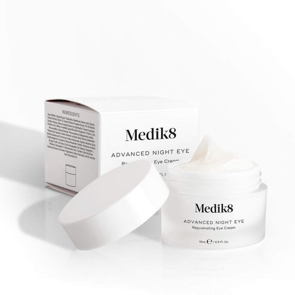 Otvorený kelímok očného krému Medik8 Advanced Night Eye Cream stojí vedľa svojho obalu na bielom pozadí. Text zvýrazňuje jeho omladzujúcu receptúru „Rejuvenating Eye Cream“ a objem 15 ml.
