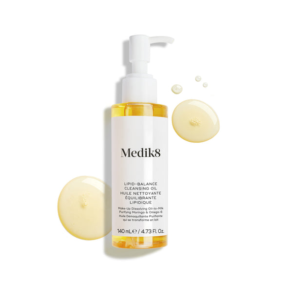 Fľaštička Medik8 Lipid-Balance Cleansing Oil stojí na bielom pozadí. Fľaštičku obklopujú zlaté kvapôčky oleja, ktoré zvýrazňujú jeho bohatú, tekutú textúru.-24