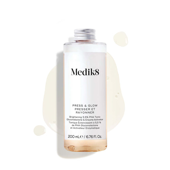 200 ml číra náhradná fľaštička exfoliačného tonika Medik8 Press & Glow so strieborným skrutkovacím viečkom. Fľaštička je umiestnená na bielom pozadí medzi kalužou a kvapôčkami bledožltého tonika, ktoré zvýrazňujú jeho tekutú textúru.-42
